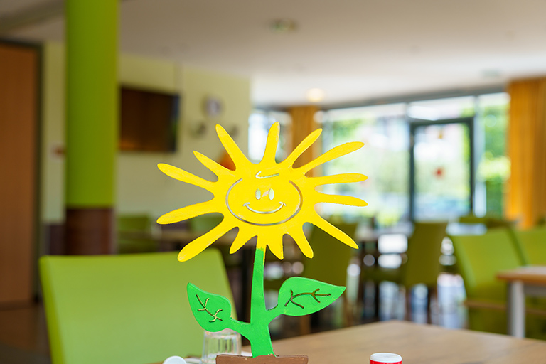 Auf dem Tisch steht ein Blümchen, das wie eine Sonne aussieht.